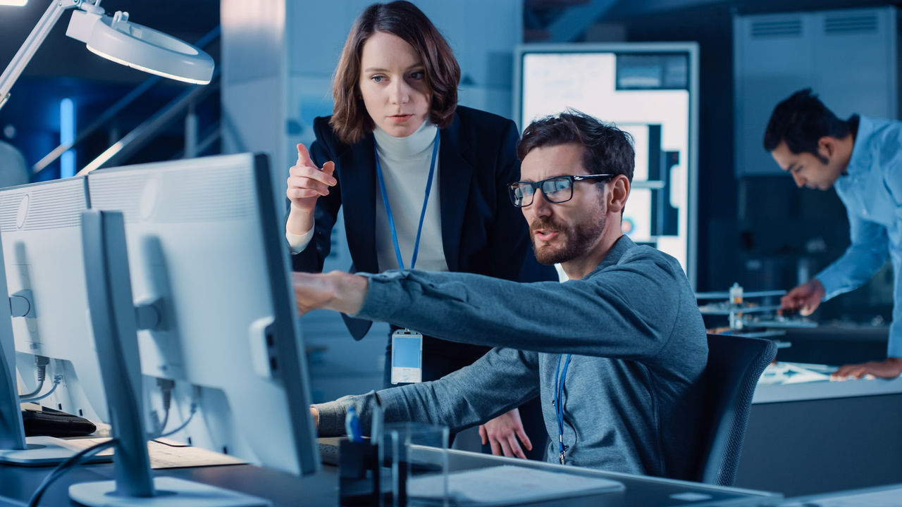 Futuristic Machine Engine Development Engineer Working on Computer at His Desk, Talks with Female Project Manager. Team of Professionals Working in the Modern Industrial Design Institution