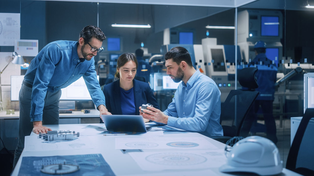 Factory Office Meeting Room: Team of Engineers Gather Around Conference Table, They Discuss Project Blueprints, Inspect Mechanism, Find Solutions, Use Laptop. Industrial Technology Factory