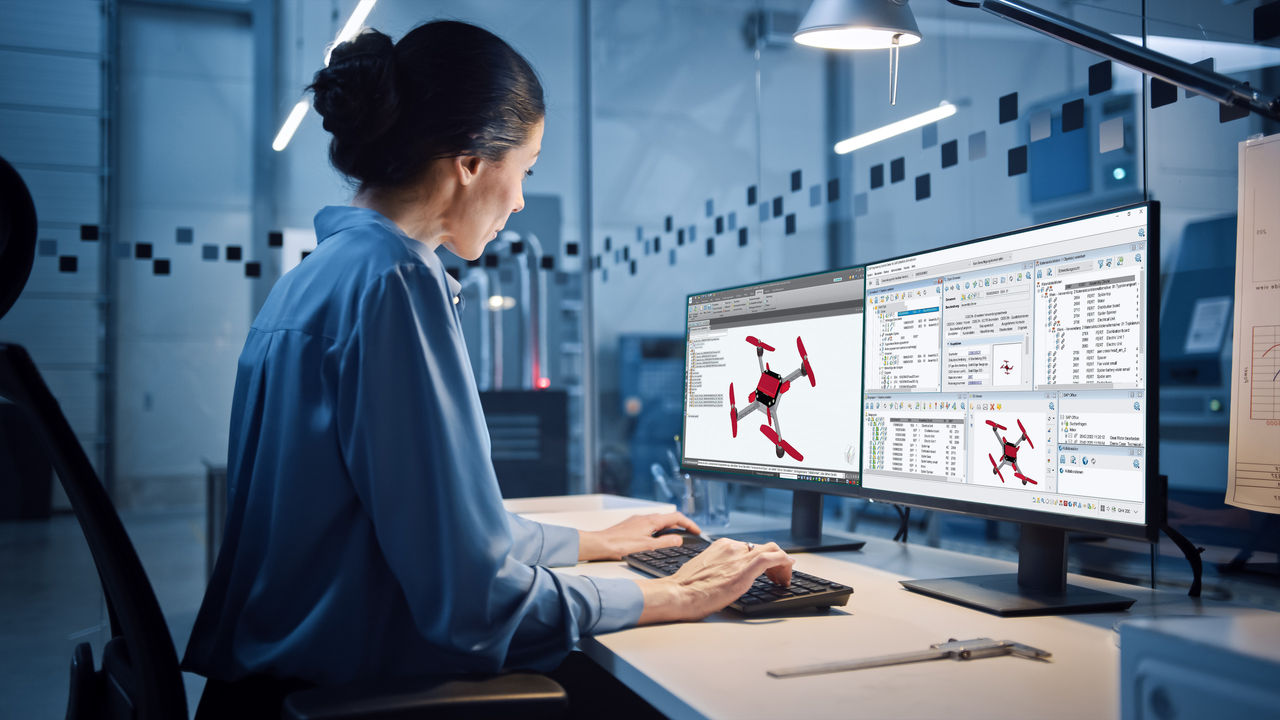 Portrait of Young and Confident Industrial Engineer Working on Computer, on Screen CAD Software Showing New Generation Electric Engine. Industrial Factory with High-Tech CNC Machinery.